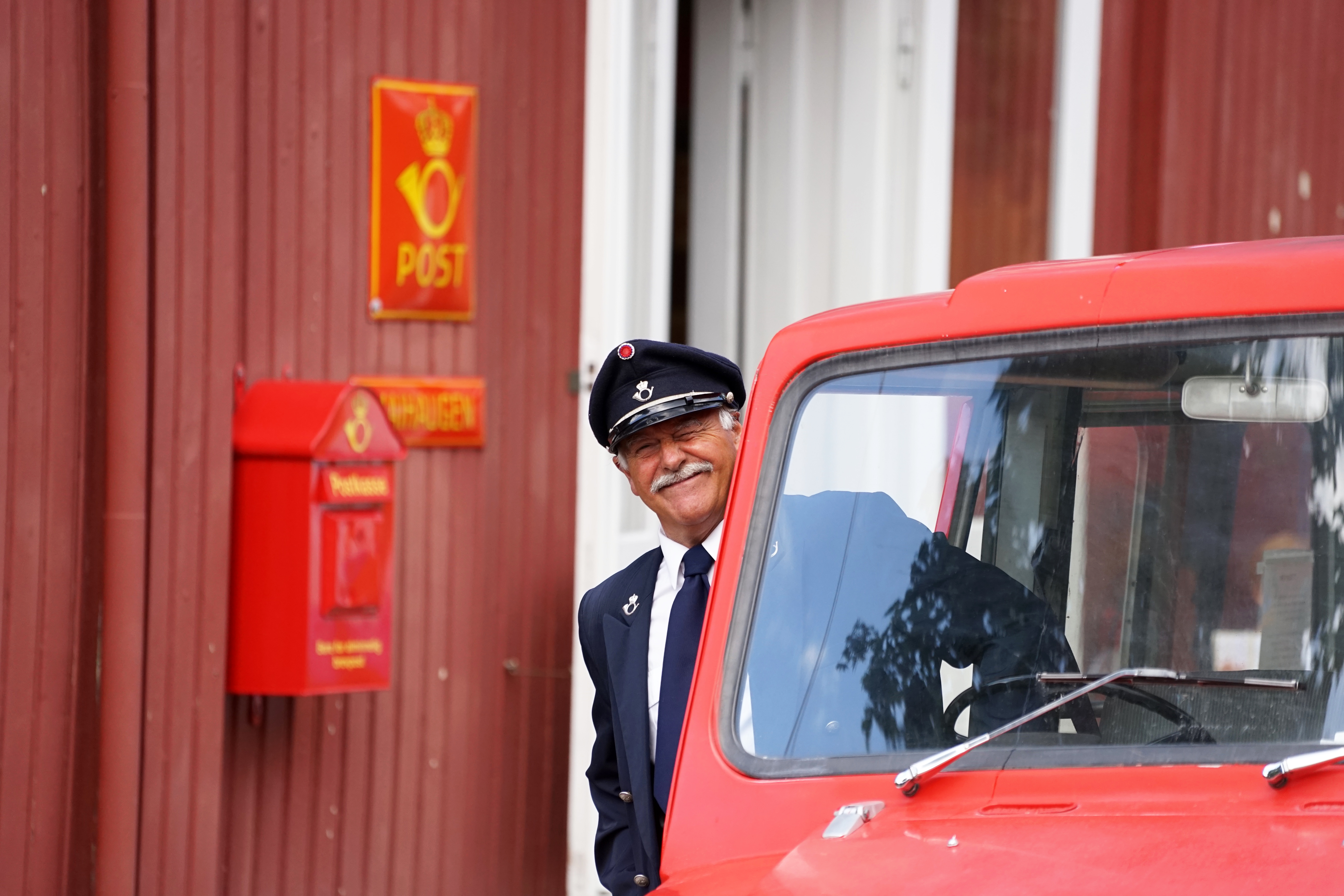 Postmann ved postbil blunker med øyet.